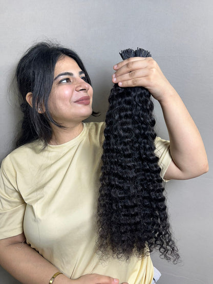 Curly human hair I-tip extension bundle held upright, dark black ringlets